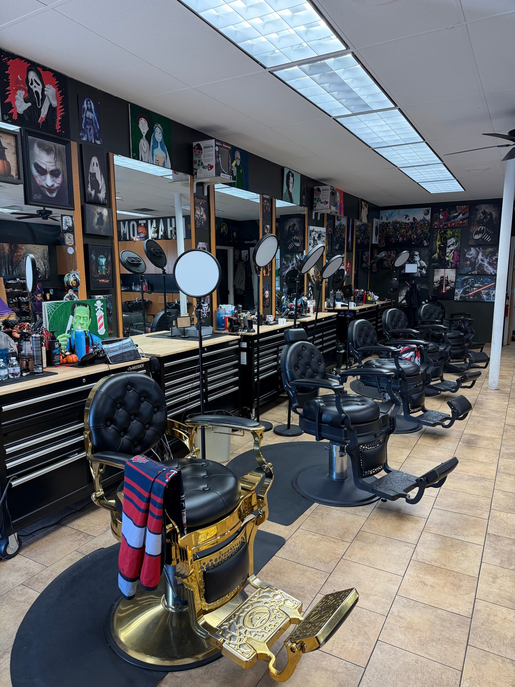 Phantom Fades cutting floor — antique gold-base barber chair in the foreground, premium stations and pop-culture art lining the walls